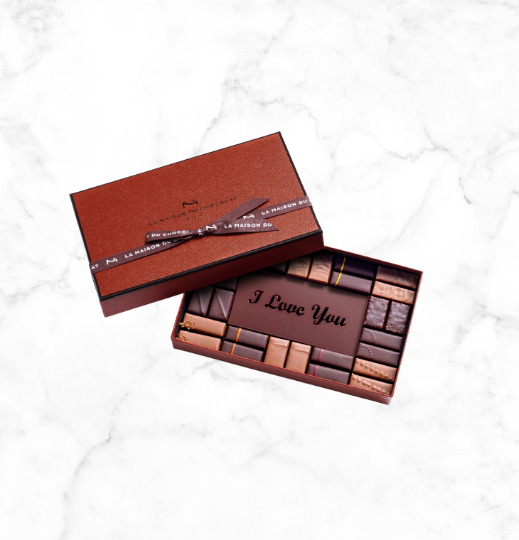 A mix of our 16 signature flavors, including an assortment of milk and dark chocolate pralines and ganache elegantly covered by an engraved dark chocolate plaque showing “I Love You”.