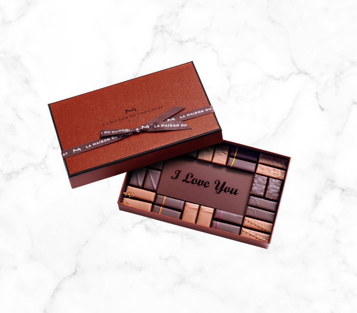 A mix of our 16 signature flavors, including an assortment of milk and dark chocolate pralines and ganache elegantly covered by an engraved dark chocolate plaque showing “I Love You”.