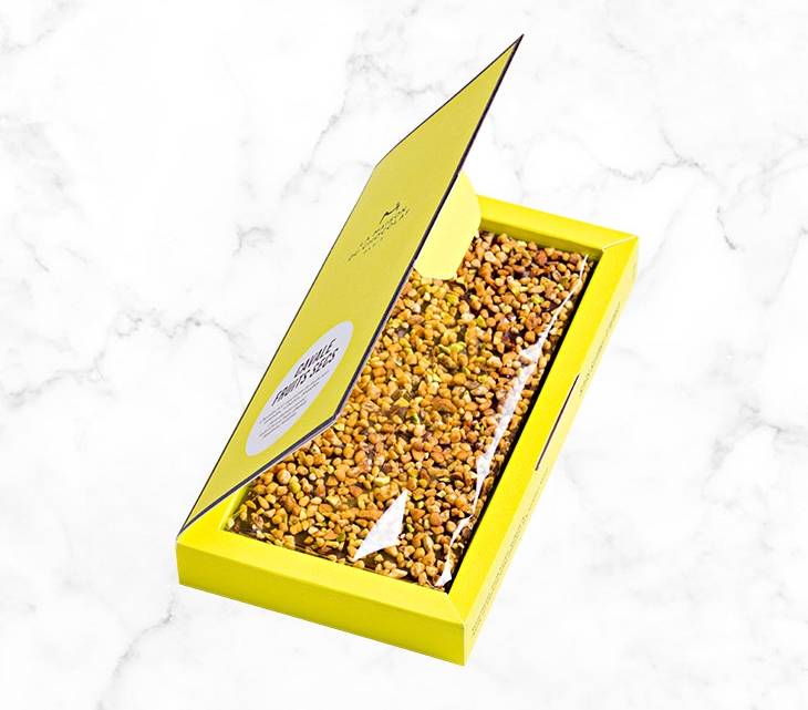 A crunchy mixture of almonds, pistachios and hazelnuts on a thin layer of dark chocolate, creating the perfect bar to share, presented in an elegant and brightly colored box.