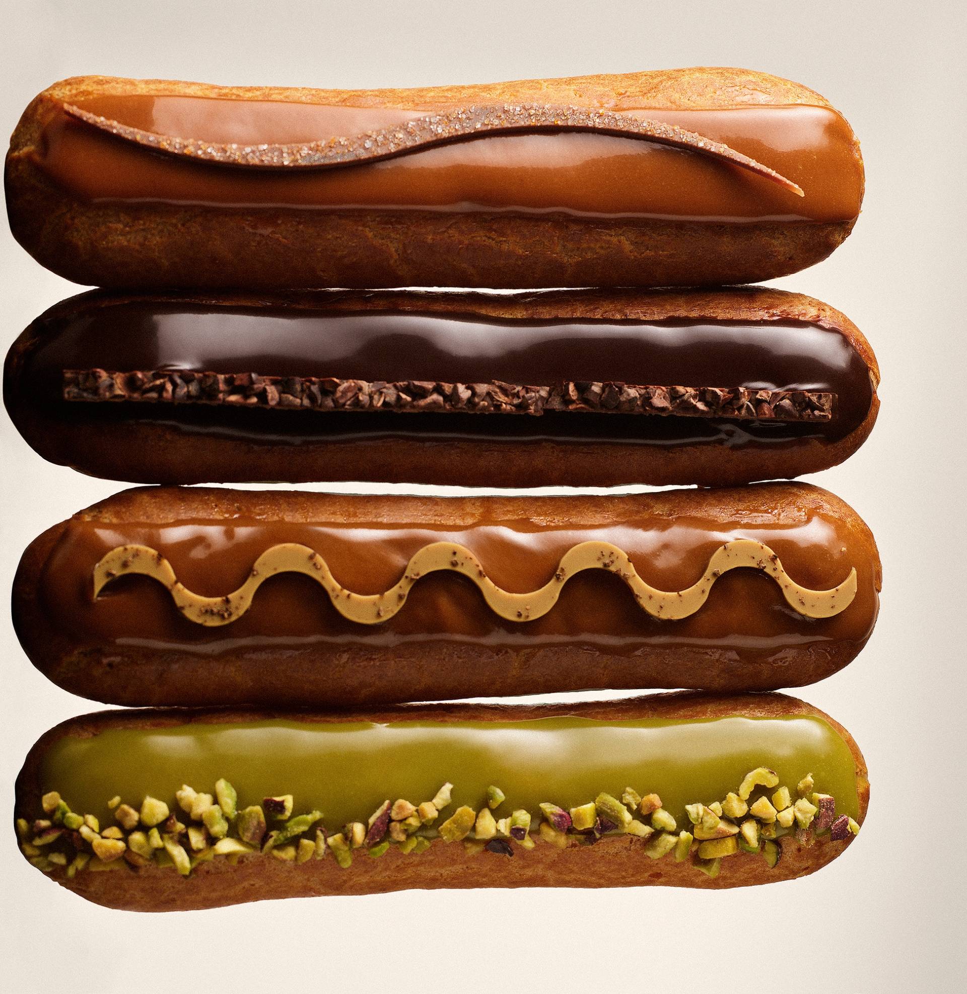 various maison eclairs arranged in row with flavors of chocolate, caramel, coffee, and pistachio displayed against a beige background